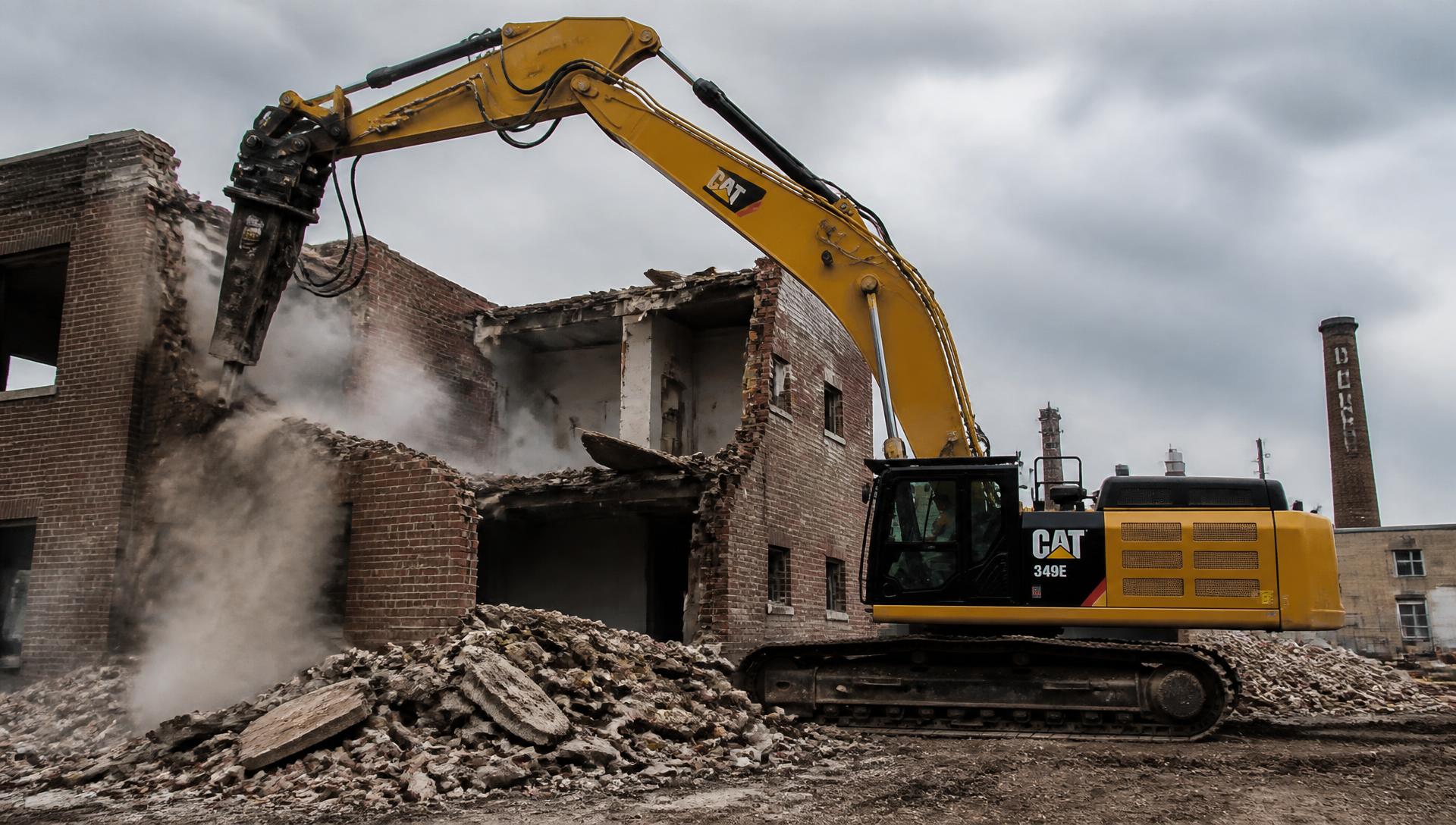 Excavator with hydraulic breaker demolishing a brick building at a Boston job site
